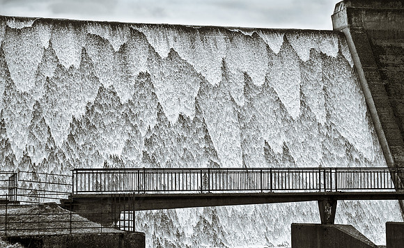 "cascading water down reservoir spillway with pedestrian bridge in foreground", "water infrastructure"