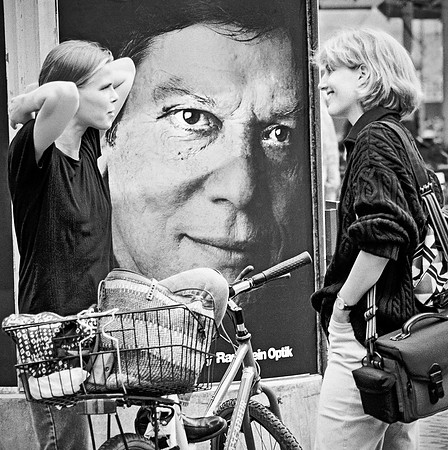 " advertising bollard with riveting stare of man between two ladies in conversation"